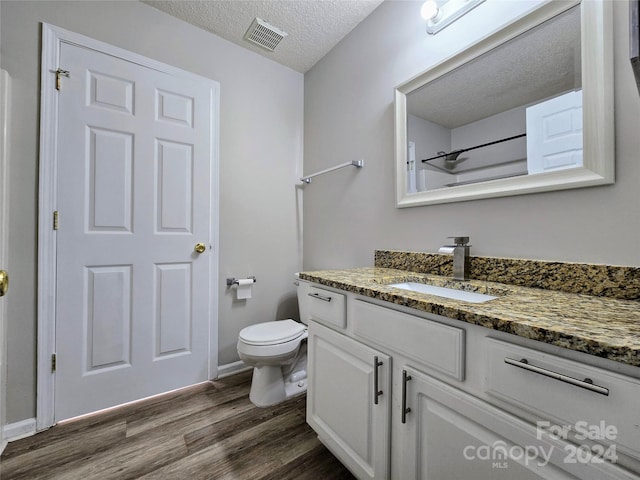 bathroom with hardwood / wood-style flooring, a textured ceiling, vanity, and toilet