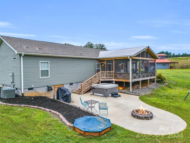 rear view of house featuring a lawn, cooling unit, an outdoor fire pit, a sunroom, and a hot tub