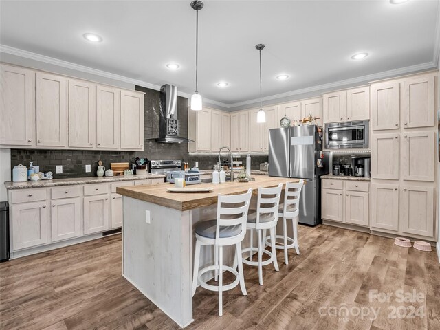 kitchen featuring light wood-type flooring, appliances with stainless steel finishes, a kitchen island with sink, backsplash, and wall chimney range hood