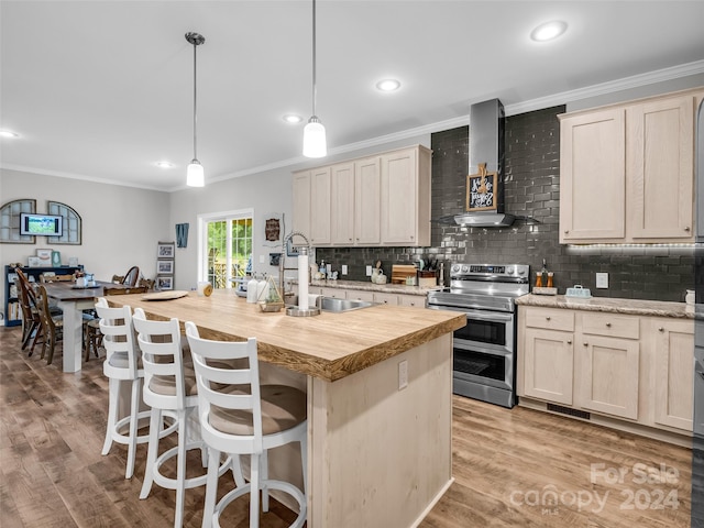 kitchen with pendant lighting, sink, wall chimney range hood, double oven range, and a center island with sink