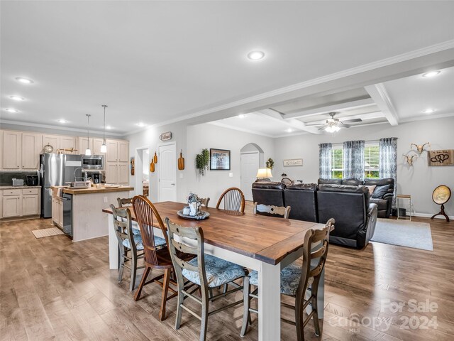 dining area featuring ceiling fan, ornamental molding, coffered ceiling, beamed ceiling, and light wood-type flooring