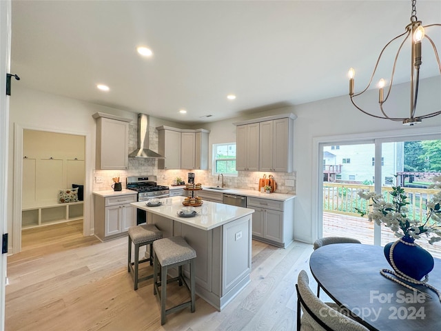 kitchen with appliances with stainless steel finishes, decorative light fixtures, gray cabinetry, a center island, and wall chimney range hood