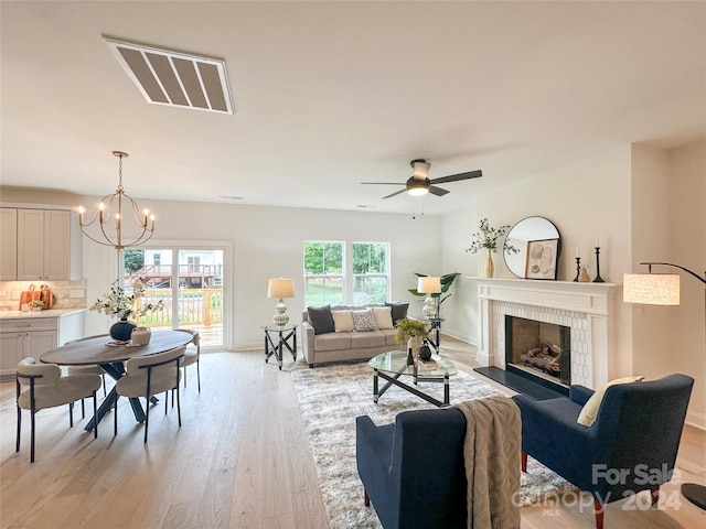 living room with a tile fireplace, ceiling fan with notable chandelier, and light hardwood / wood-style floors