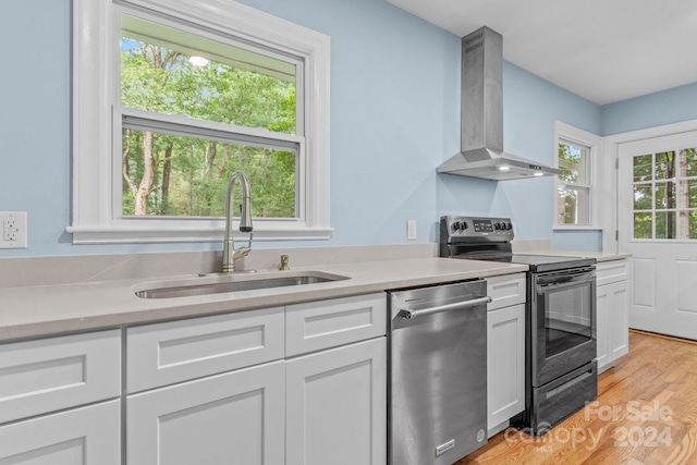 kitchen featuring stainless steel dishwasher, light wood-type flooring, wall chimney exhaust hood, electric range, and sink