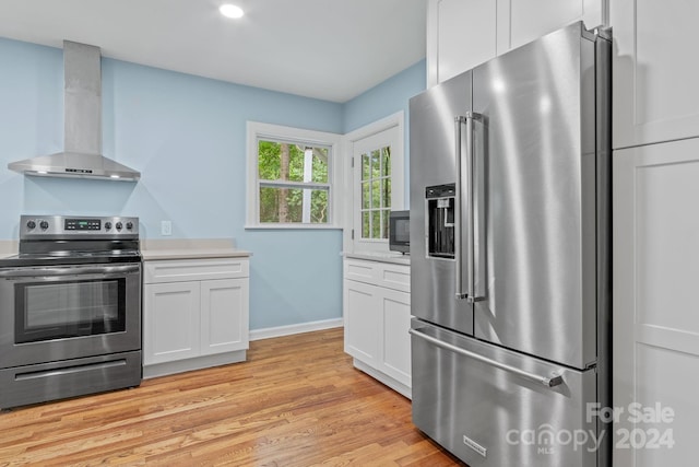 kitchen with white cabinetry, stainless steel appliances, light hardwood / wood-style flooring, and wall chimney range hood