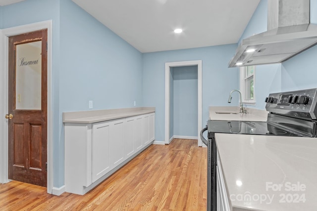 kitchen featuring white cabinetry, electric range, wall chimney range hood, light hardwood / wood-style floors, and sink