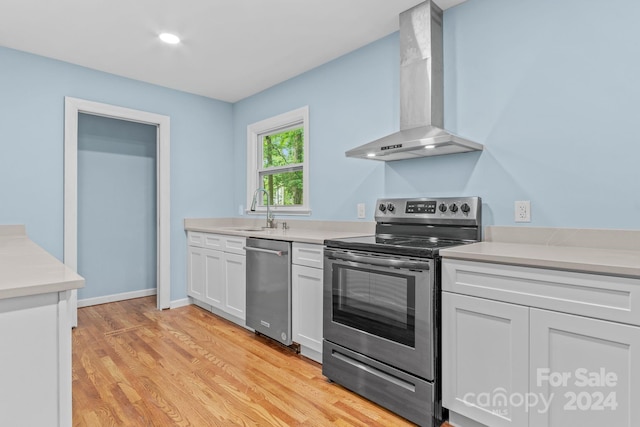 kitchen with white cabinetry, light wood-type flooring, wall chimney range hood, stainless steel appliances, and sink