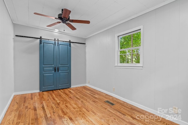 unfurnished bedroom with light wood-type flooring, crown molding, a barn door, and ceiling fan