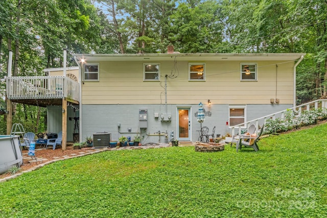 back of property with a fire pit, a deck, and a lawn