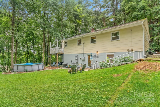 rear view of property featuring a pool side deck, cooling unit, and a lawn