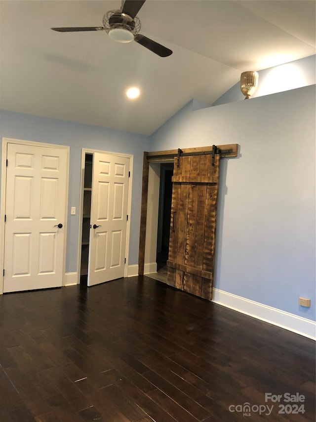 unfurnished living room with a barn door, ceiling fan, dark hardwood / wood-style floors, and vaulted ceiling