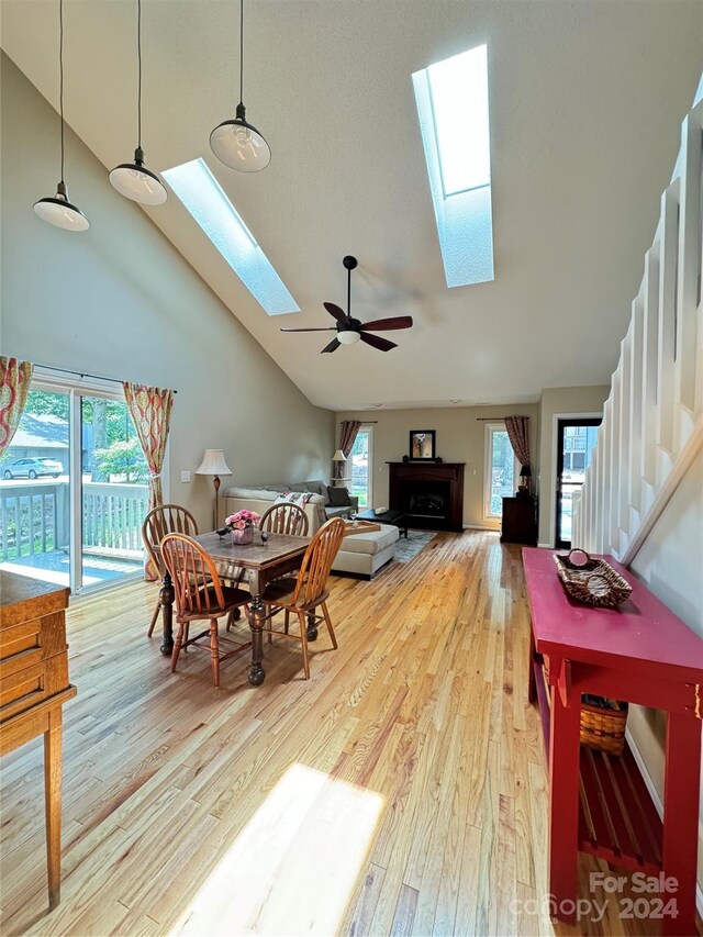 dining room featuring ceiling fan, high vaulted ceiling, a skylight, and light hardwood / wood-style flooring