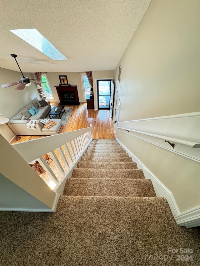 stairway featuring hardwood / wood-style flooring, a textured ceiling, a skylight, and a healthy amount of sunlight