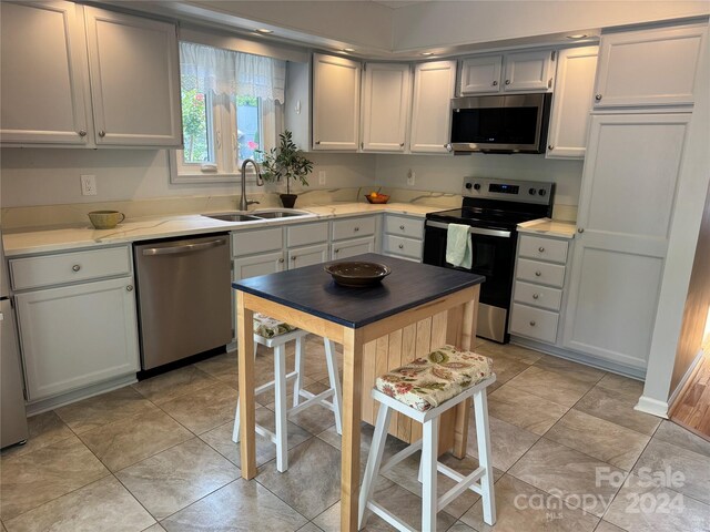 kitchen featuring appliances with stainless steel finishes, light stone counters, light tile patterned floors, and sink