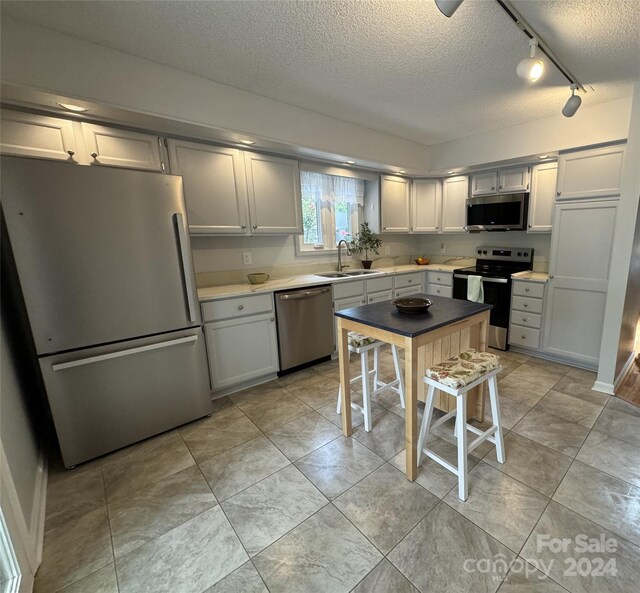 kitchen with sink, stainless steel appliances, a textured ceiling, and light tile patterned floors