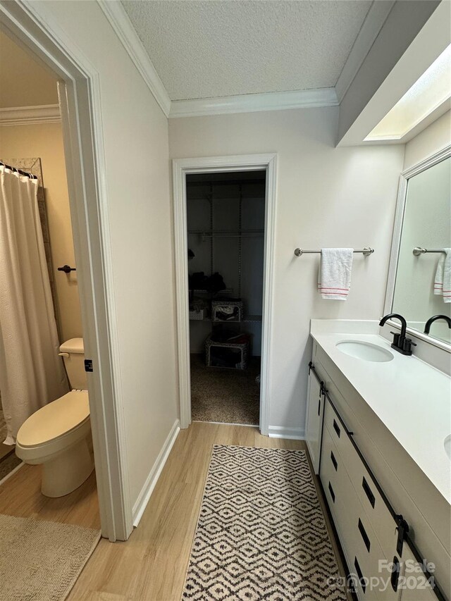 bathroom with vanity, crown molding, a textured ceiling, wood-type flooring, and toilet