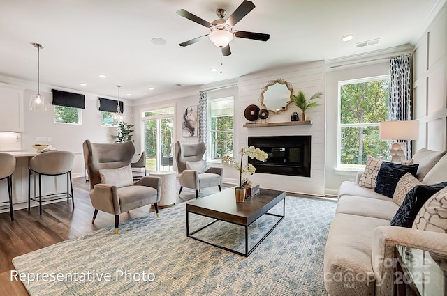 living room with crown molding, dark hardwood / wood-style floors, a large fireplace, and ceiling fan