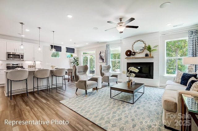 living room featuring ceiling fan, a wealth of natural light, a fireplace, and light wood-type flooring