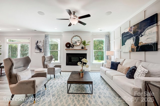 living room featuring a fireplace, ornamental molding, ceiling fan, and light wood-type flooring