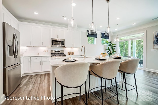 kitchen featuring appliances with stainless steel finishes, dark hardwood / wood-style floors, pendant lighting, white cabinetry, and an island with sink