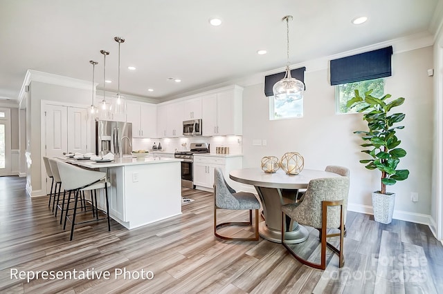 kitchen featuring appliances with stainless steel finishes, pendant lighting, white cabinetry, a center island with sink, and light hardwood / wood-style flooring