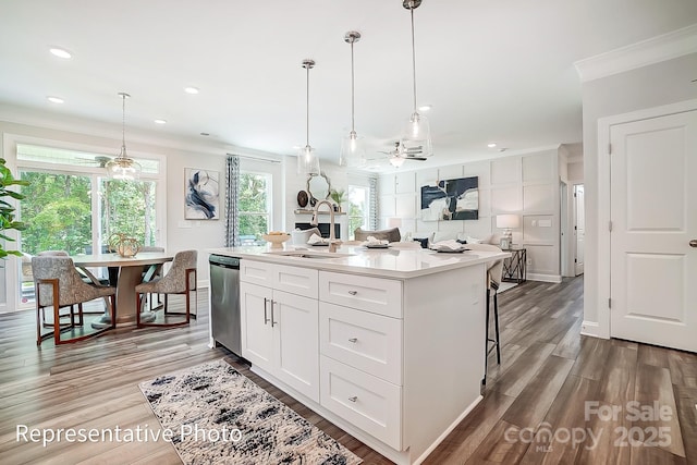 kitchen with decorative light fixtures, white cabinetry, sink, a kitchen island with sink, and light hardwood / wood-style flooring