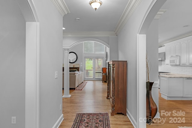 hallway featuring crown molding, light hardwood / wood-style flooring, and decorative columns