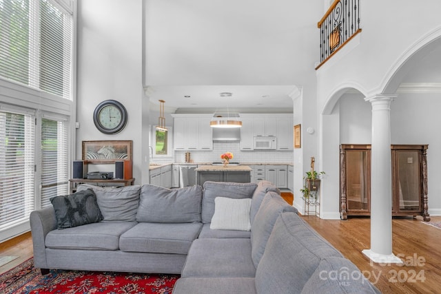 living room featuring sink, decorative columns, a high ceiling, ornamental molding, and light hardwood / wood-style floors