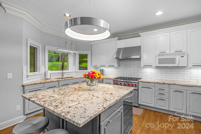 kitchen with pendant lighting, wall chimney range hood, sink, and a center island