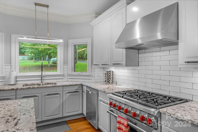 kitchen with pendant lighting, high end stove, sink, crown molding, and wall chimney range hood