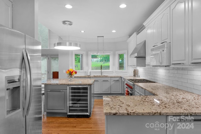 kitchen with pendant lighting, gray cabinetry, beverage cooler, stainless steel appliances, and wall chimney exhaust hood