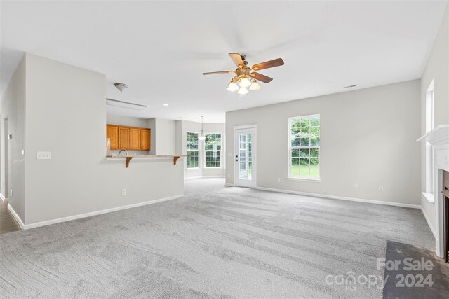 unfurnished living room with light colored carpet and ceiling fan