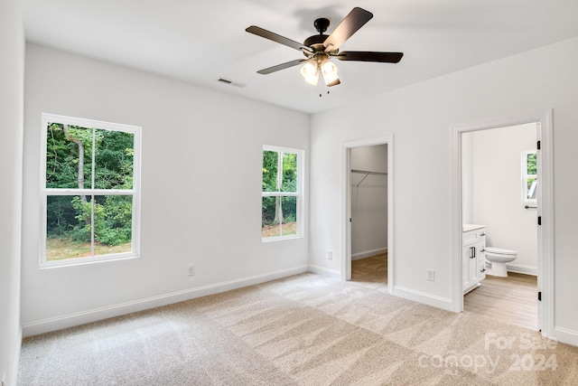 unfurnished bedroom featuring a closet, connected bathroom, ceiling fan, a walk in closet, and light carpet