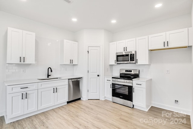 kitchen with sink, appliances with stainless steel finishes, white cabinets, and light wood-type flooring