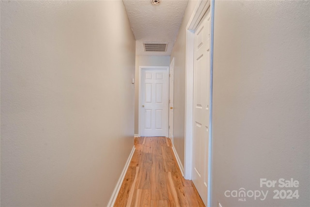 hallway with a textured ceiling and light wood-type flooring