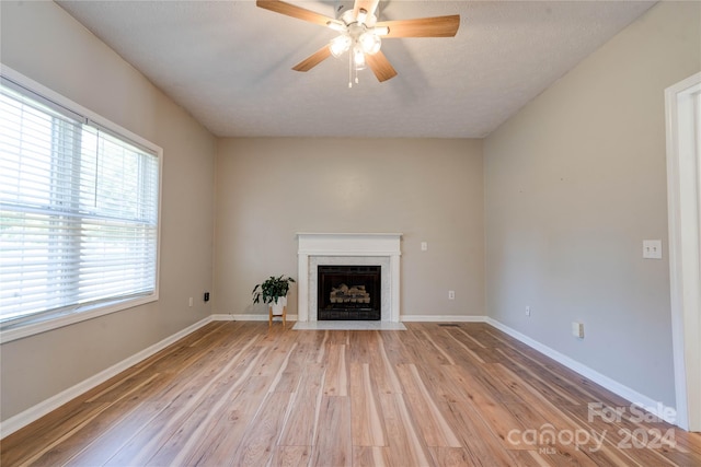 unfurnished living room with ceiling fan, a textured ceiling, a high end fireplace, and light hardwood / wood-style flooring