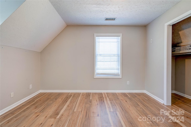 bonus room with lofted ceiling, light hardwood / wood-style floors, and a textured ceiling