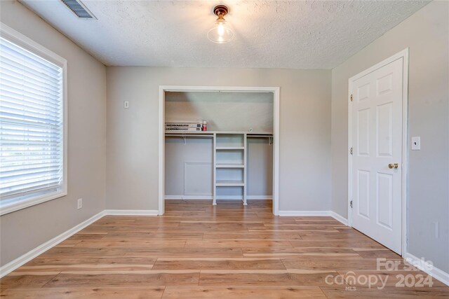 unfurnished bedroom featuring a closet, a textured ceiling, and light wood-type flooring