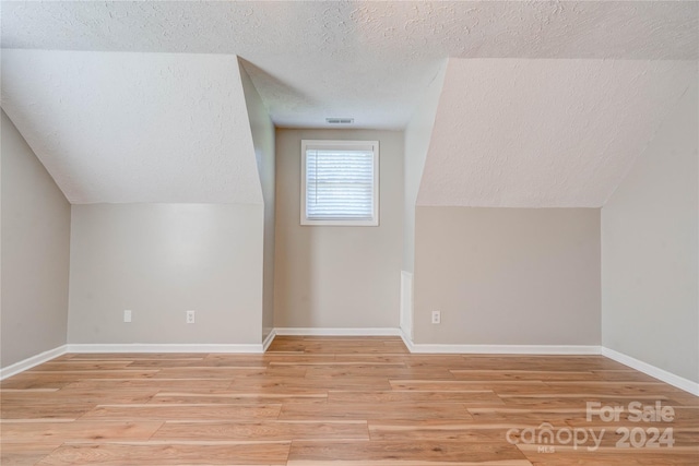 bonus room featuring vaulted ceiling, light hardwood / wood-style floors, and a textured ceiling