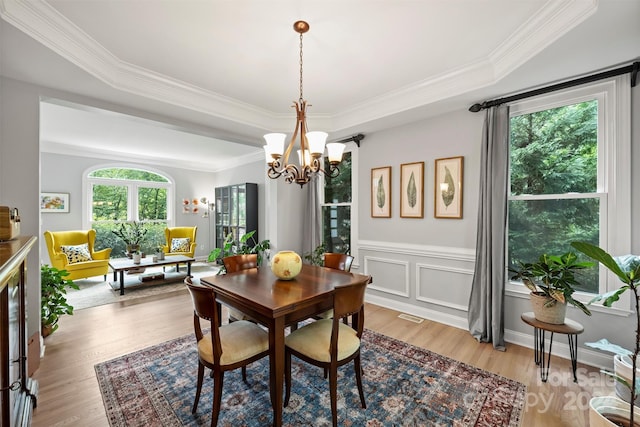 dining area with light wood-type flooring, a raised ceiling, and a wealth of natural light