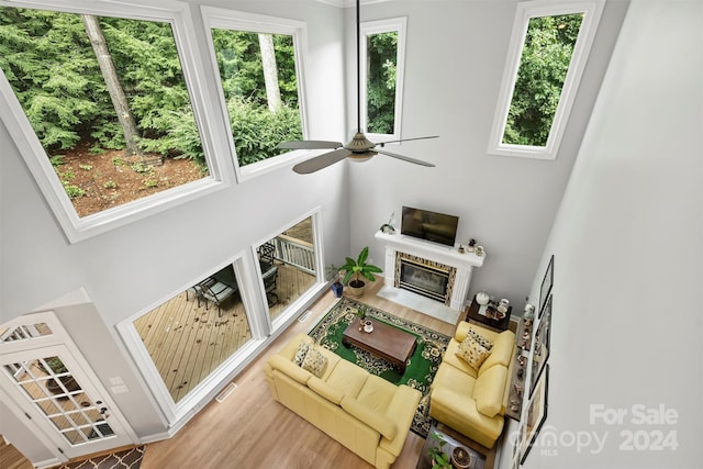 living room with ceiling fan, light hardwood / wood-style floors, a high end fireplace, and a high ceiling