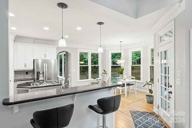 kitchen with white cabinetry, light hardwood / wood-style flooring, tasteful backsplash, appliances with stainless steel finishes, and pendant lighting