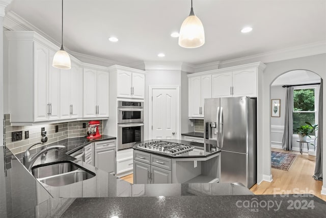 kitchen with tasteful backsplash, stainless steel appliances, sink, hanging light fixtures, and light wood-type flooring