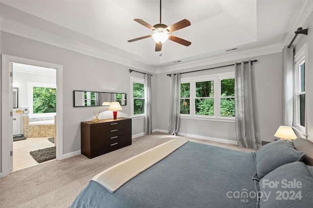 bedroom featuring crown molding, ceiling fan, a tray ceiling, light colored carpet, and ensuite bath