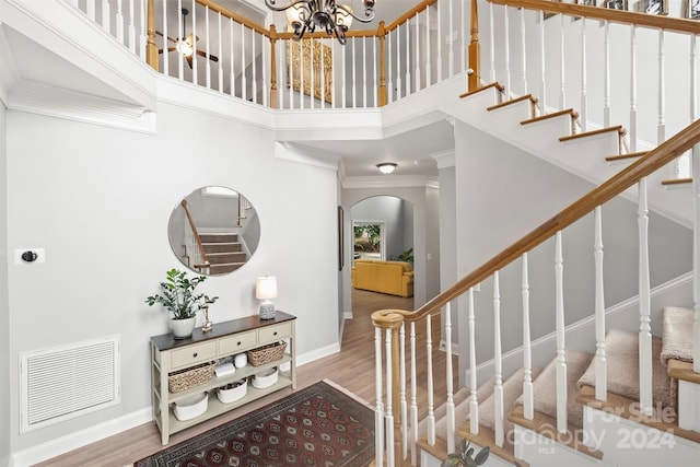 stairs featuring ornamental molding, wood-type flooring, a towering ceiling, and a chandelier