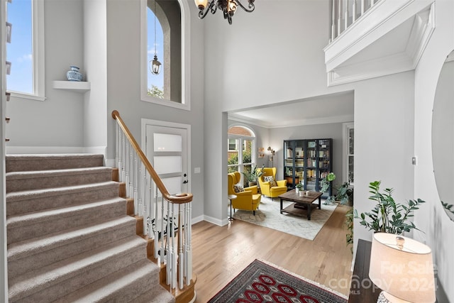 foyer with an inviting chandelier, wood-type flooring, crown molding, and a high ceiling