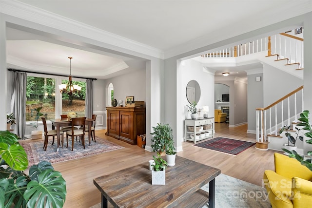 living room featuring a raised ceiling, crown molding, light wood-type flooring, and a chandelier