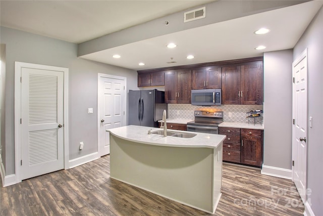 kitchen featuring a kitchen island with sink, dark hardwood / wood-style floors, backsplash, and appliances with stainless steel finishes