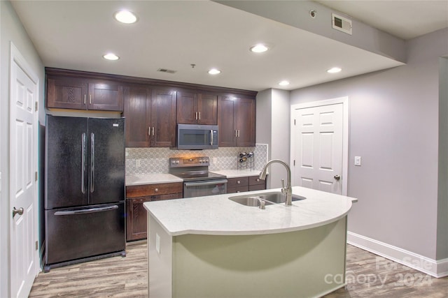 kitchen featuring stainless steel appliances, sink, light hardwood / wood-style flooring, backsplash, and a kitchen island with sink