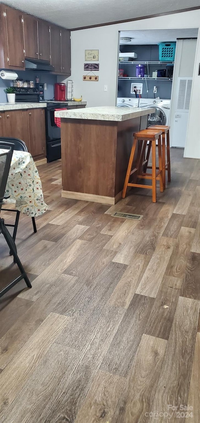 kitchen with dark brown cabinetry, a kitchen breakfast bar, light hardwood / wood-style floors, and electric range